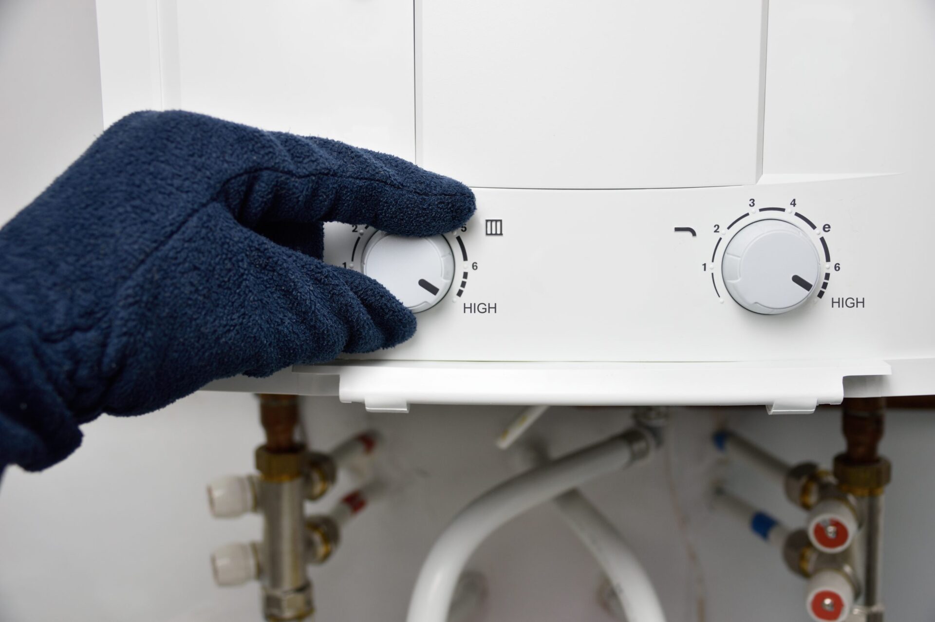 Hand with gloves on adjusting the temperature on a tankless water heater 