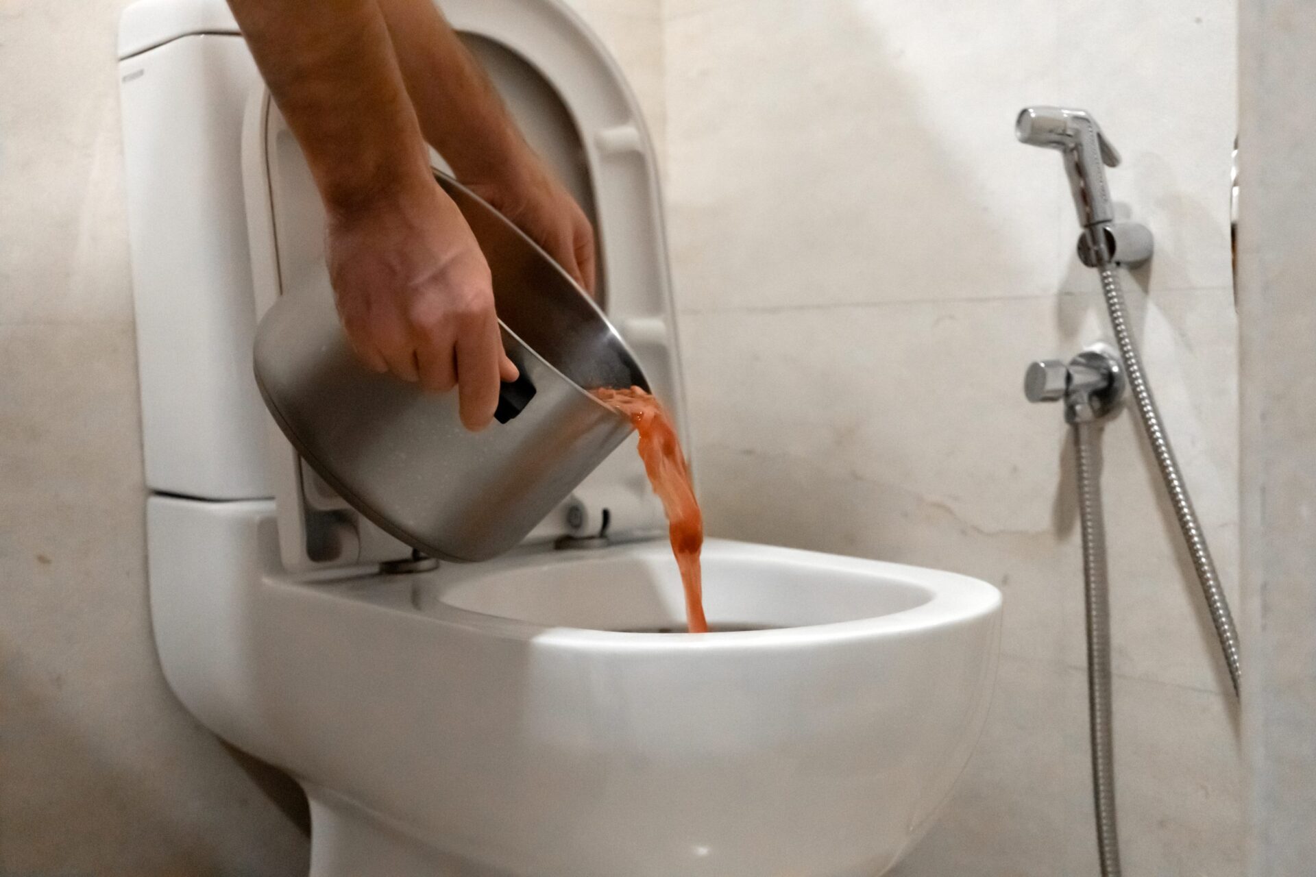 Person pouring food from a pot in the toilet causing a clogged toilet. MidCity Plumbers