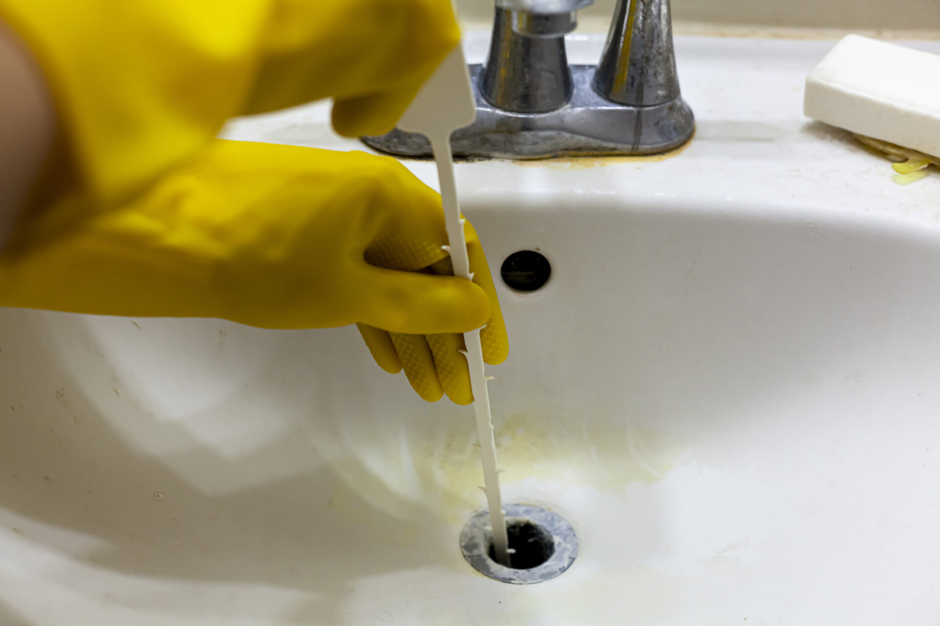 Person trying to unclog the drain of a sink using snake drain or auger tool which helps pull hair and soap debris from the sinkhole. MidCity Plumbers