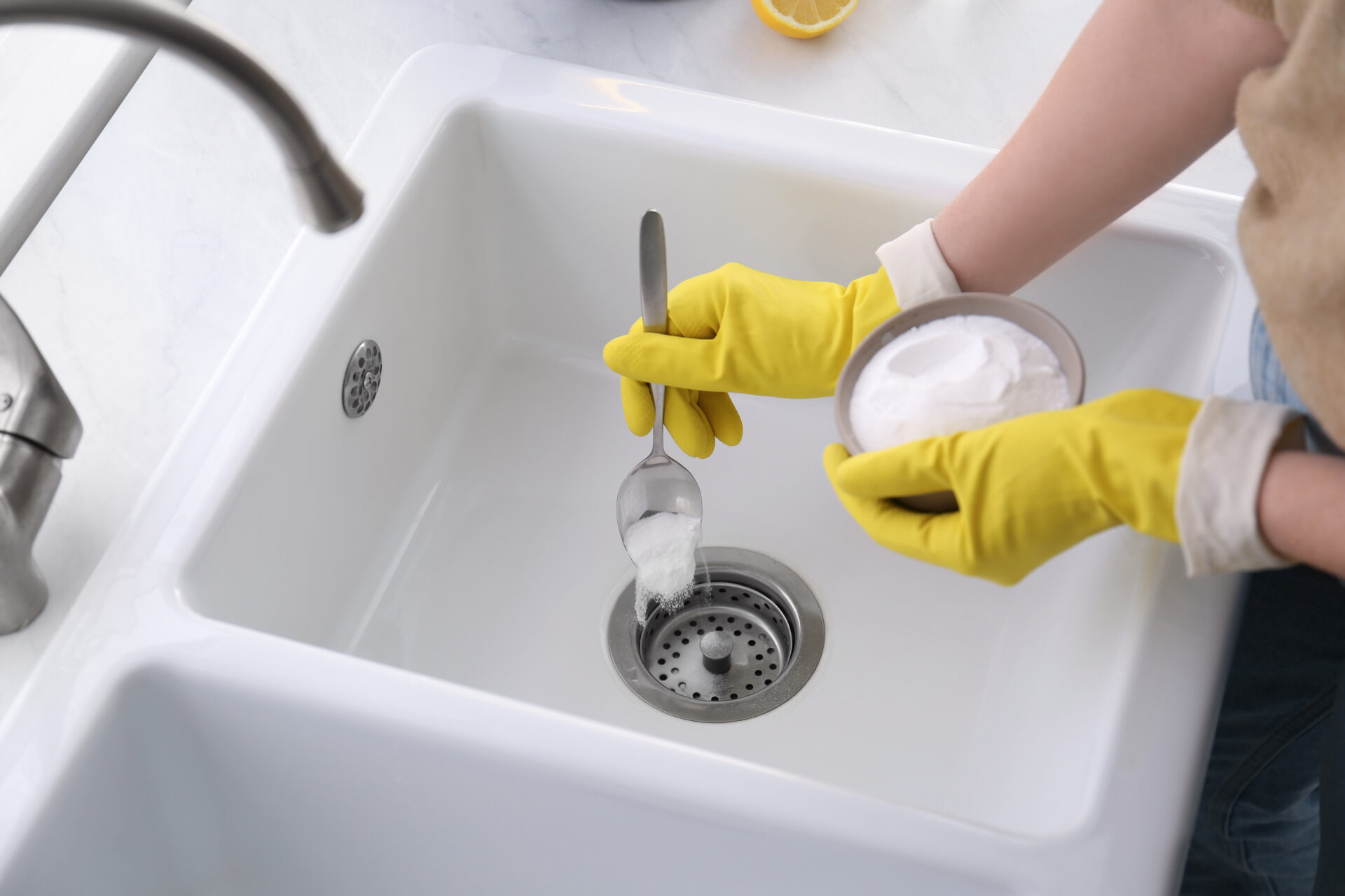 Person with yellow gloves using baking soda to unclog sink drain. MidCity Plumbers.