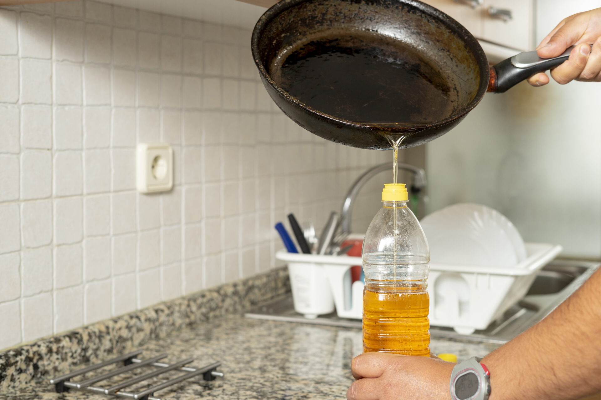 Man placing recycled used cooking oil from a frying pan into a plastic bottle in their kitchen. MidCity Plumbers.