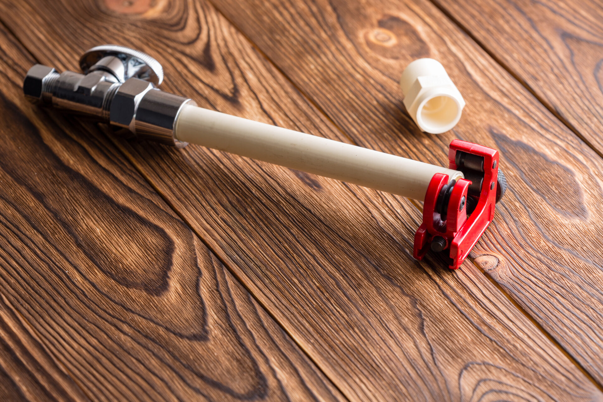 CPVC pipe for a plumbing installation or repair in a bright red pipe cutter over a wooden table. MidCity Plumbers