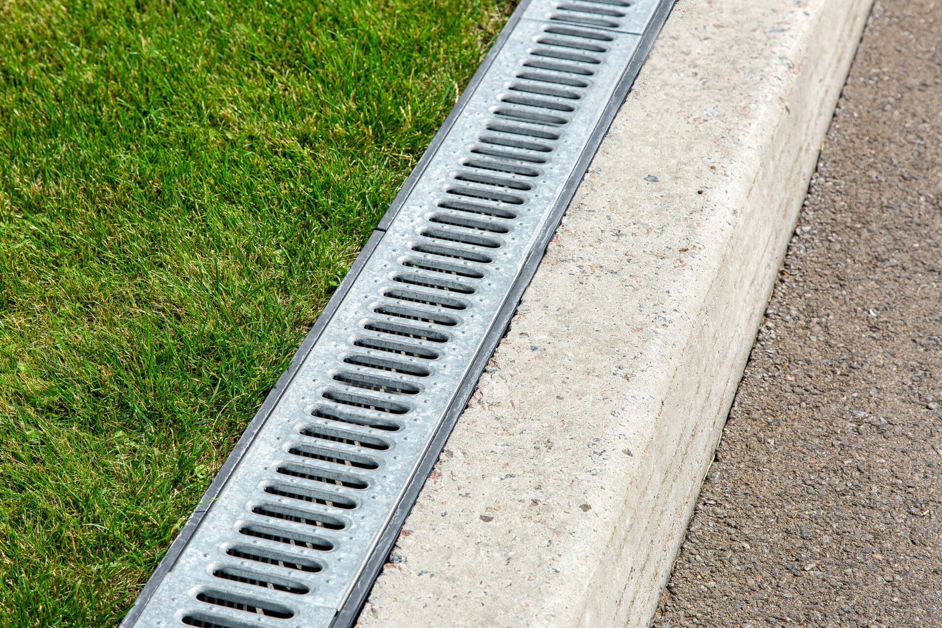 Close up of outdoor drainage in plumbing system along a asphalt road and green grass. MidCity Plumbers