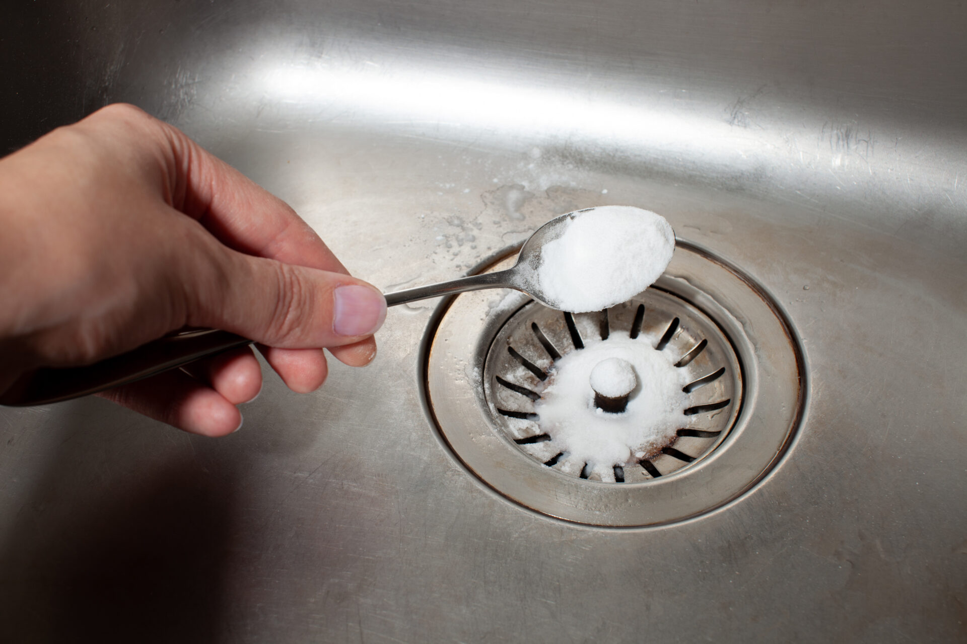 Spoonful of baking soda being poured down drain to prevent kitchen drain smells. MidCity Plumbers