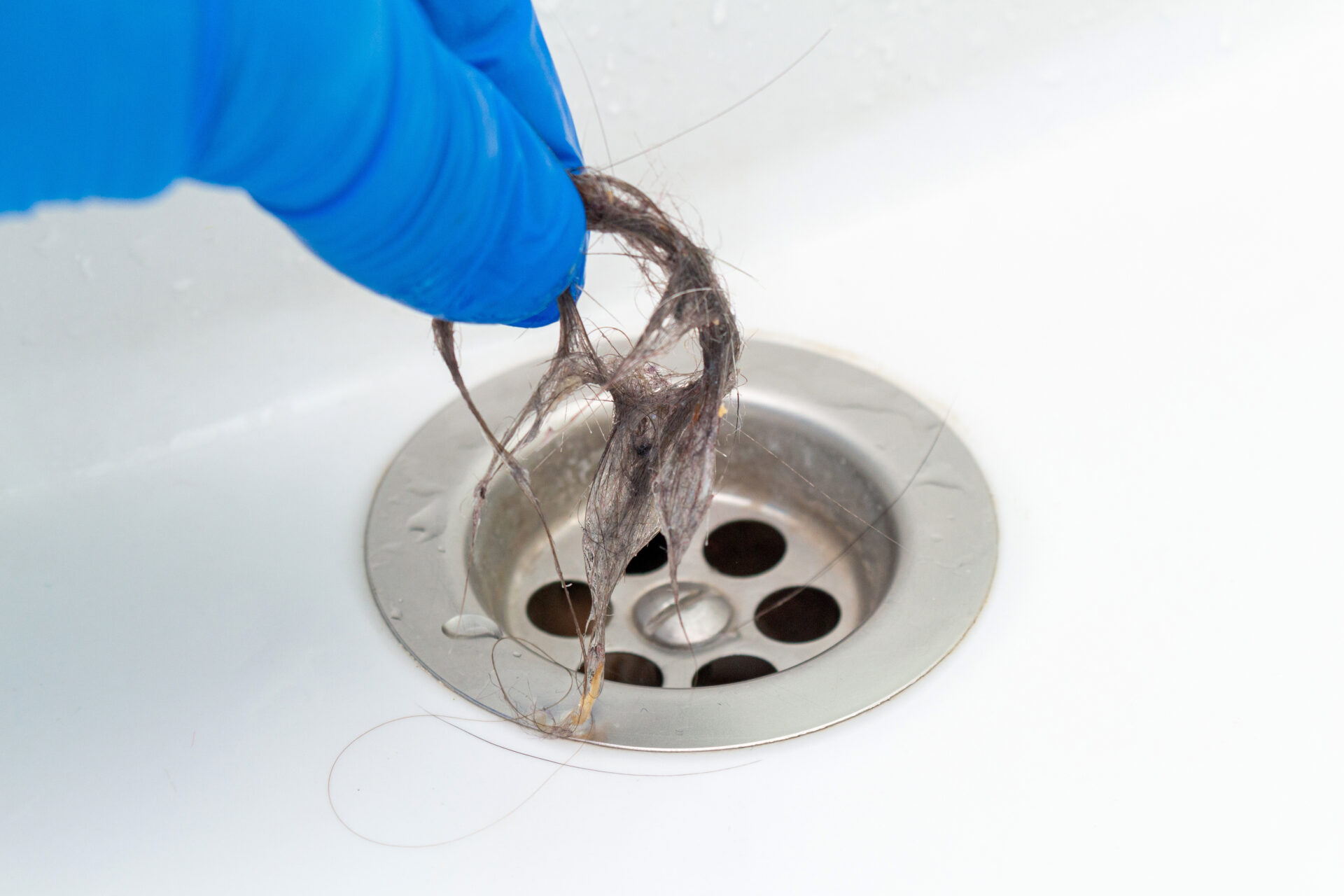 Hand in glove cleaning a clogged drain in the sink or bathtub from hair. MidCity Plumbers